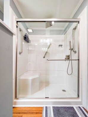 Ein modernes Badezimmer mit Glasduschtür, Handbrause, Handbrause, Handtuchhalter und einer Duschsteuerung.