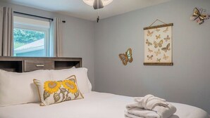 Une chambre à coucher avec un lit, des oreillers, une décoration murale représentant un papillon et une fenêtre avec des rideaux.