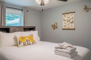 Ein Schlafzimmer mit einem Bett, Kissen, einer Wanddekoration mit Schmetterlingen und einem Fenster mit Vorhängen.