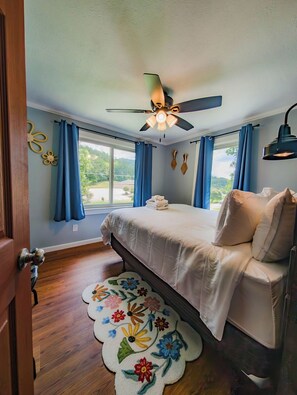 Ein Schlafzimmer mit einem Bett, einem Deckenventilator, einem Fenster mit Vorhängen, einer Tür und einem Blumenmuster-Teppich.