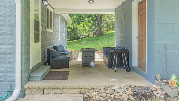 A covered porch with outdoor furniture, a trash can, and a small cart.