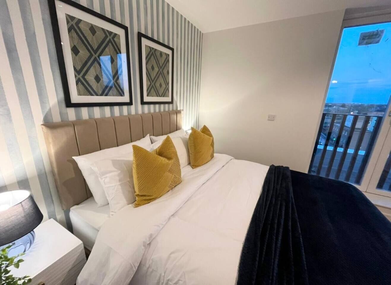 A hotel room with a bed, a nightstand, a lamp, and a window with a view.