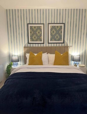 Ein Hotelzimmer mit einem Bett, gestreifter Tapete, zwei gerahmten Bildern und Nachttischlampen.