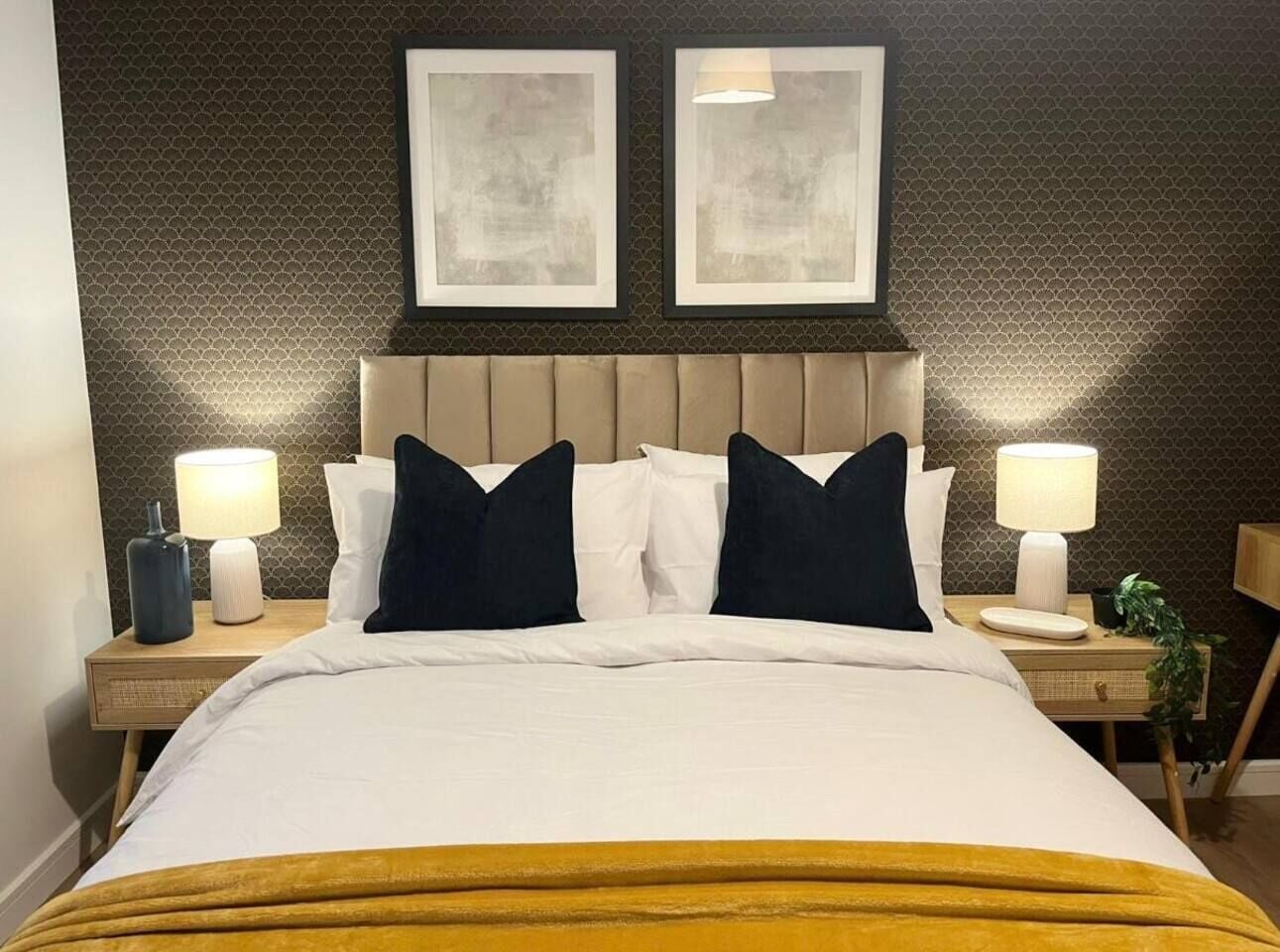 A hotel room with a bed, two bedside tables, lamps, and two framed pictures on the wall.