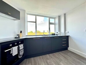 Eine moderne Küche mit Einbauofen, einem Fenster mit Ausblick und einer Arbeitsfläche mit Küchenutensilien.