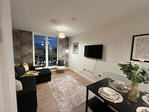Ein modernes Wohnzimmer mit einer Couch, einem Esstisch für zwei Personen und einem großen Fenster mit Blick auf die Stadt.