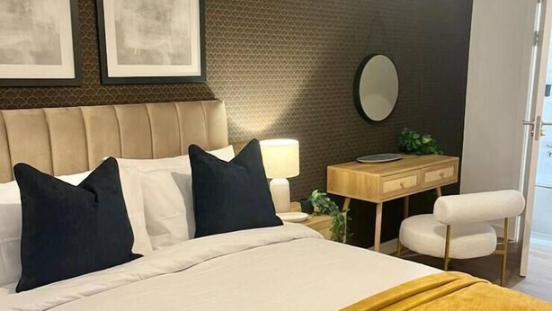 Hotellihuone, jossa on sänky, yöpöytä, tuoli ja seinälle kiinnitetty peili.