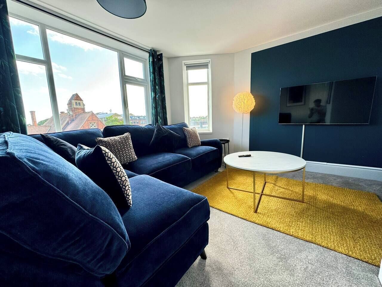 A modern living room with a blue sofa set, a round coffee table, and a flat-screen TV mounted on the wall.