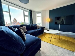 A modern living room with a blue sofa set, a round coffee table, and a flat-screen TV mounted on the wall. - #136 City Stay Near Bullring & New Street|Sleeps 6 (West Midlands)