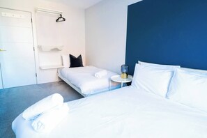 A hotel room with two beds, a small bedside table, a wall-mounted shelf, and a door. - #137 StylishApart BournemouthBeach&Pier| for 10 (Bournemouth)