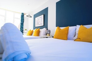 A hotel room with two beds, a bedside table, a lamp, and a window with curtains. - #137 StylishApart BournemouthBeach&Pier| for 10 (Bournemouth)
