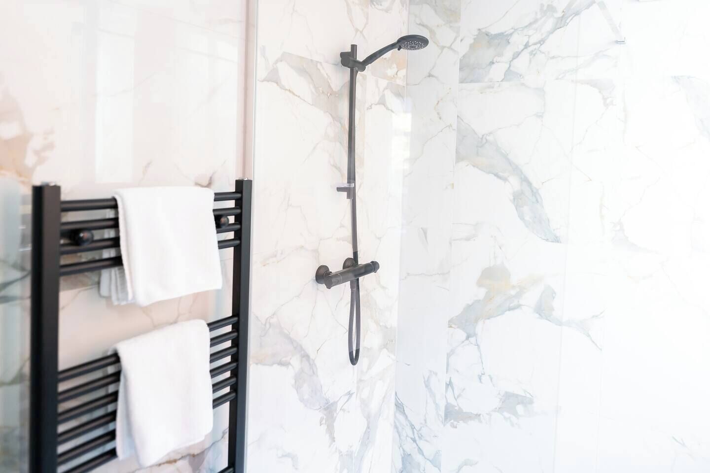 A bathroom with a black towel rack holding two towels, a black showerhead, and a marble wall.
