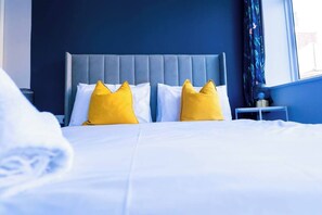Habitació d'hotel amb un llit, dos coixins, una tauleta de nit i una finestra amb cortines.