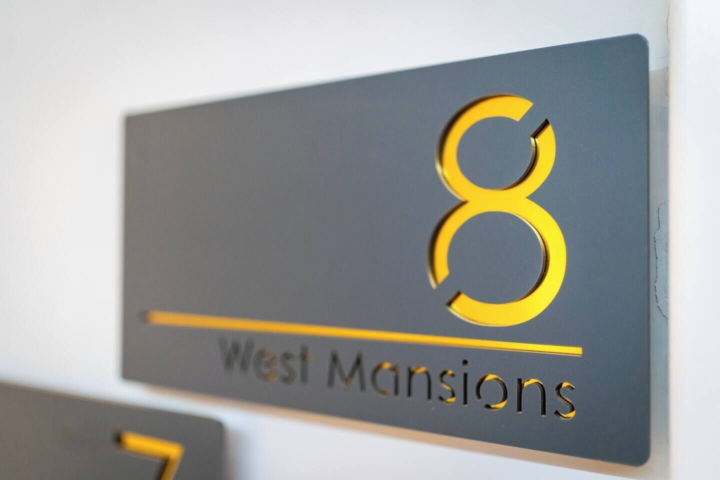 Un panneau indiquant le numéro « 8 » et le texte « West Mansions », désignant un immeuble ou un lieu.