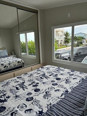 Ein Schlafzimmer mit großem Fenster, einem Bett mit gemustertem Überwurf und Blick auf eine Wohngegend.