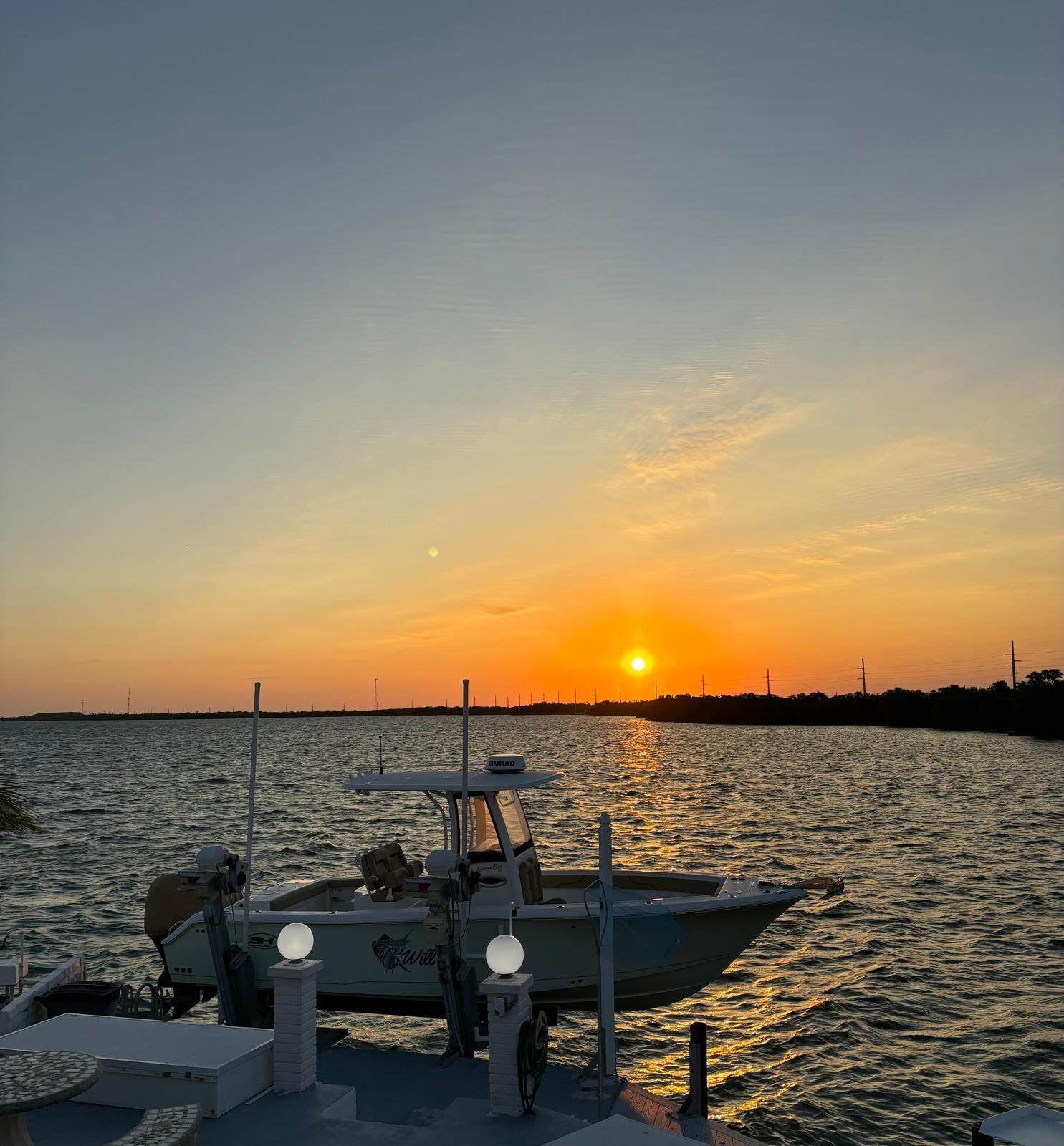 Ein Boot liegt an einem Steg, im Hintergrund ein Sonnenuntergang.