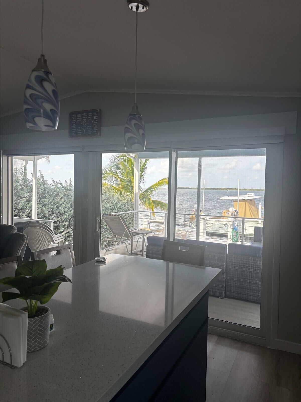 Eine moderne Küche mit einer großen Kochinsel, einem Essbereich mit Stühlen und Blick auf das Meer und Boote durch große Fenster.