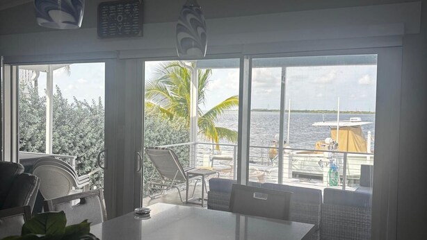 A modern kitchen with a large island, a dining area with chairs, and a view of the sea and boats through large windows. - 2-bedroom modular home in wonderful Long Key with beautiful ocean views/sunsets (Layton)