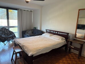 A bedroom with a bed, a chair, a bedside table, and a window with curtains. - Ocean Views Studio Apartment with Secure Parking, walk to shops and the beach. (St Kilda)