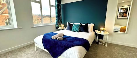 Hotelkamer met een bed, nachtkastje, lamp en uitzicht op gebouwen.