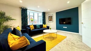 A modern living room with a sofa, coffee table, and a flat-screen TV mounted on the wall. - #139 Large coastal apartment near Beach|sleeps 10 (Bournemouth)