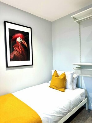 A single bed with white bedding and a yellow pillow, a framed picture of a bird on the wall, and a metal shelf unit. - #139 Large coastal apartment near Beach|sleeps 10 (Bournemouth)