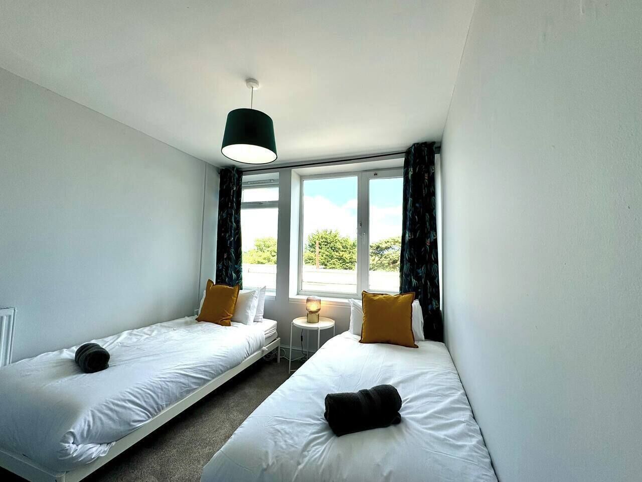Habitación de hotel con dos camas individuales, una mesita, una lámpara y una ventana con cortinas.