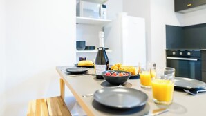 A modern kitchen with a dining table set for breakfast, including a bottle of wine, a bowl of fruit, and a glass of orange juice. - #139 Large coastal apartment near Beach|sleeps 10 (Bournemouth)