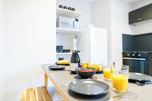 Eine moderne Küche mit Esstisch, gedeckt für ein Frühstück, inklusive einer Weinflasche, einer Obstschale und einem Glas Orangensaft.