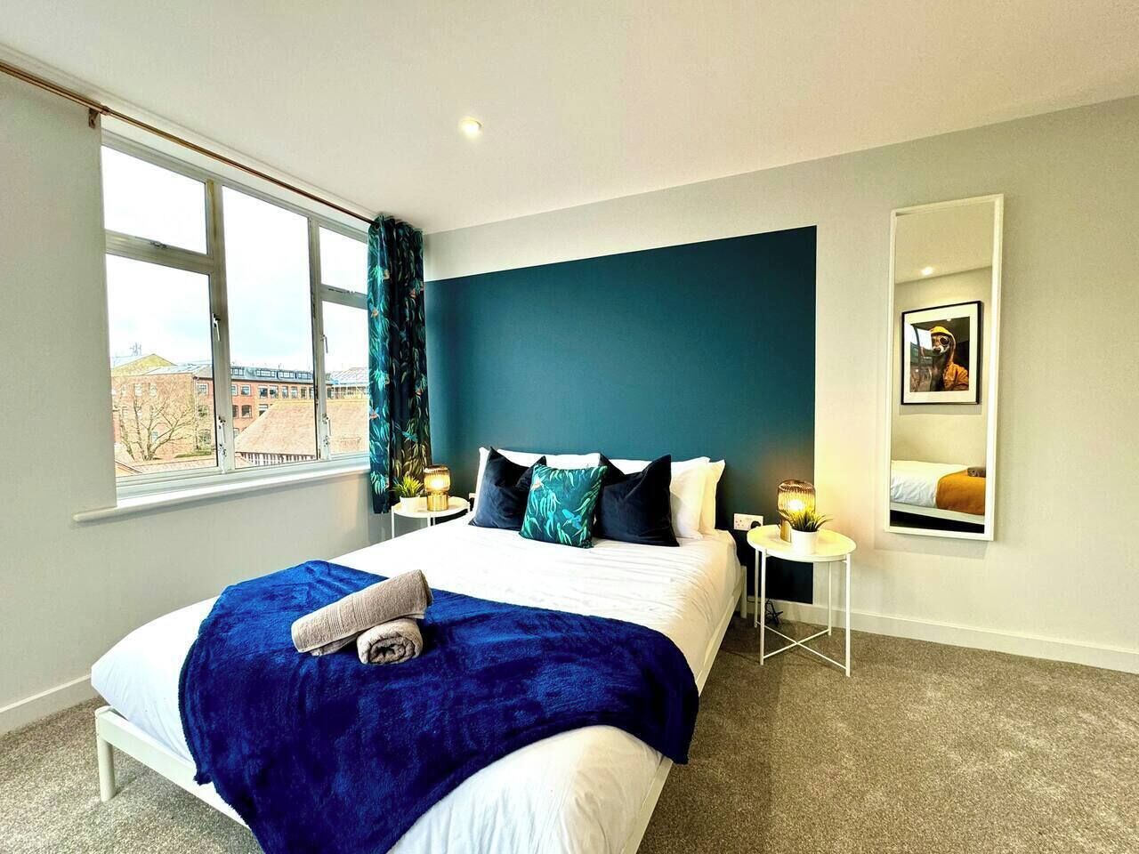 Een moderne hotelkamer met een groot bed, een nachtkastje, een spiegel en een raam met gordijnen.