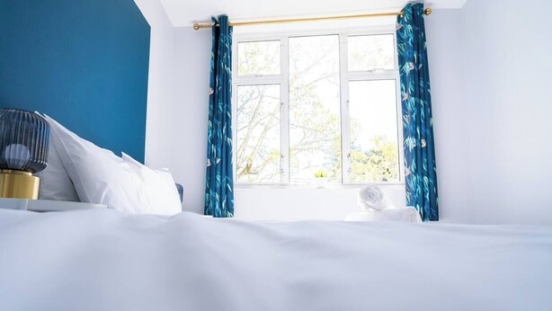 A hotel room with a bed, a bedside table, a lamp, and a window with curtains. - #139 Large coastal apartment near Beach|sleeps 10 (Bournemouth)