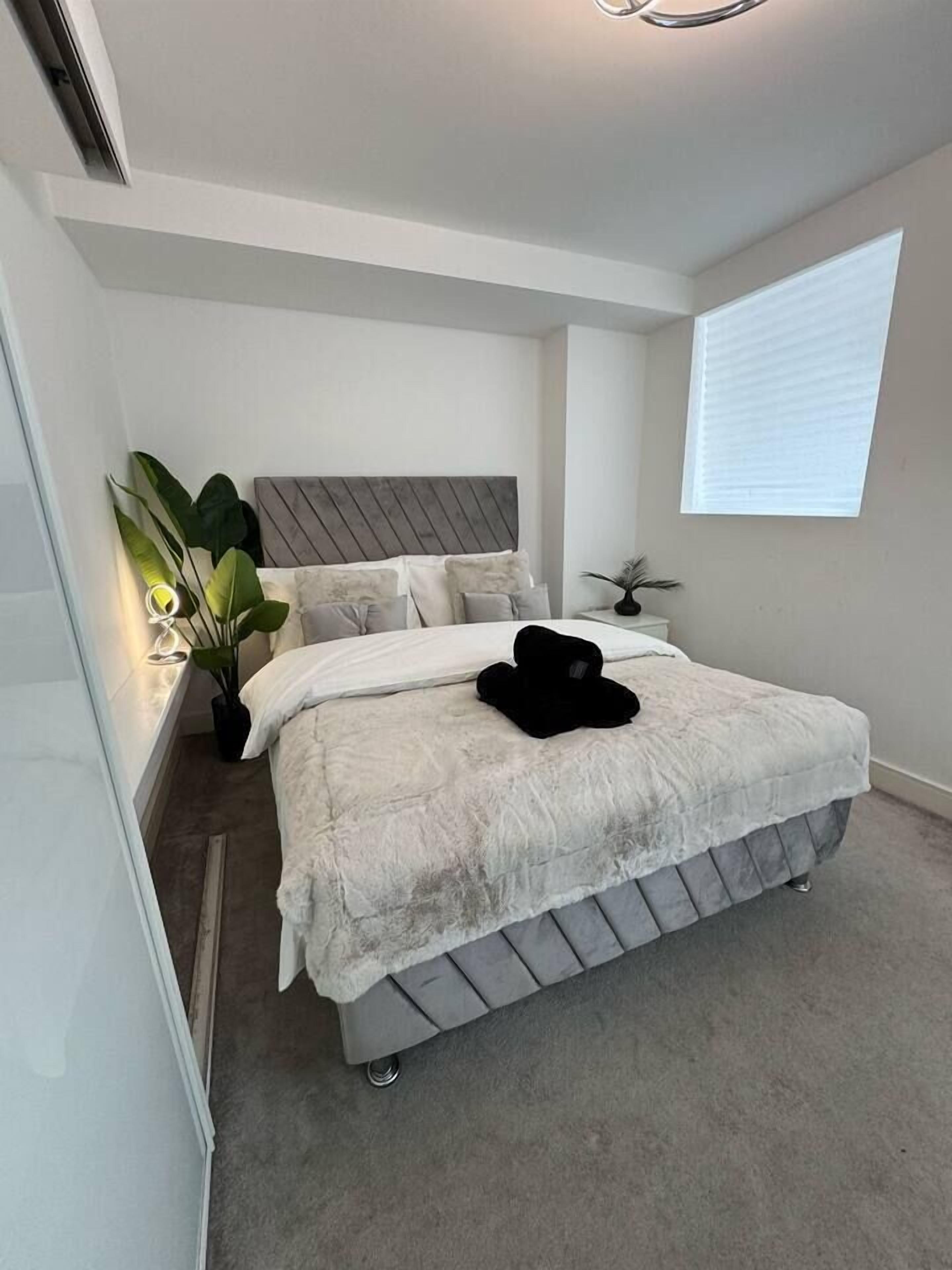 A bedroom with a bed, a bedside plant, and a window.