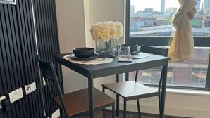 Uma sala de jantar com uma mesa, cadeiras, um vaso com flores e vista para a cidade pela janela.