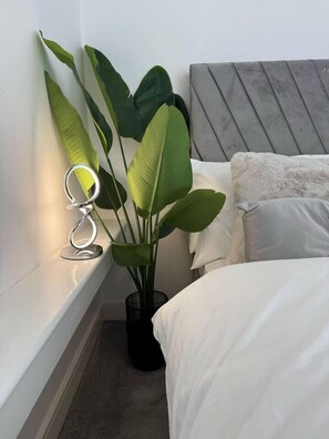Ein Schlafzimmer mit einem Bett, einem Kopfteil, einer Zimmerpflanze und einer Ringlampe auf einem Regal.