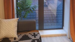 Um quarto com uma janela ampla, uma planta e uma almofada estampada.