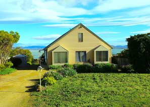 A single-story house with a gabled roof, a front porch, and a view of the ocean.