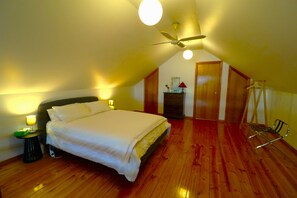 A bedroom with a single bed, a nightstand, a lamp, a ceiling fan, and a wooden floor.