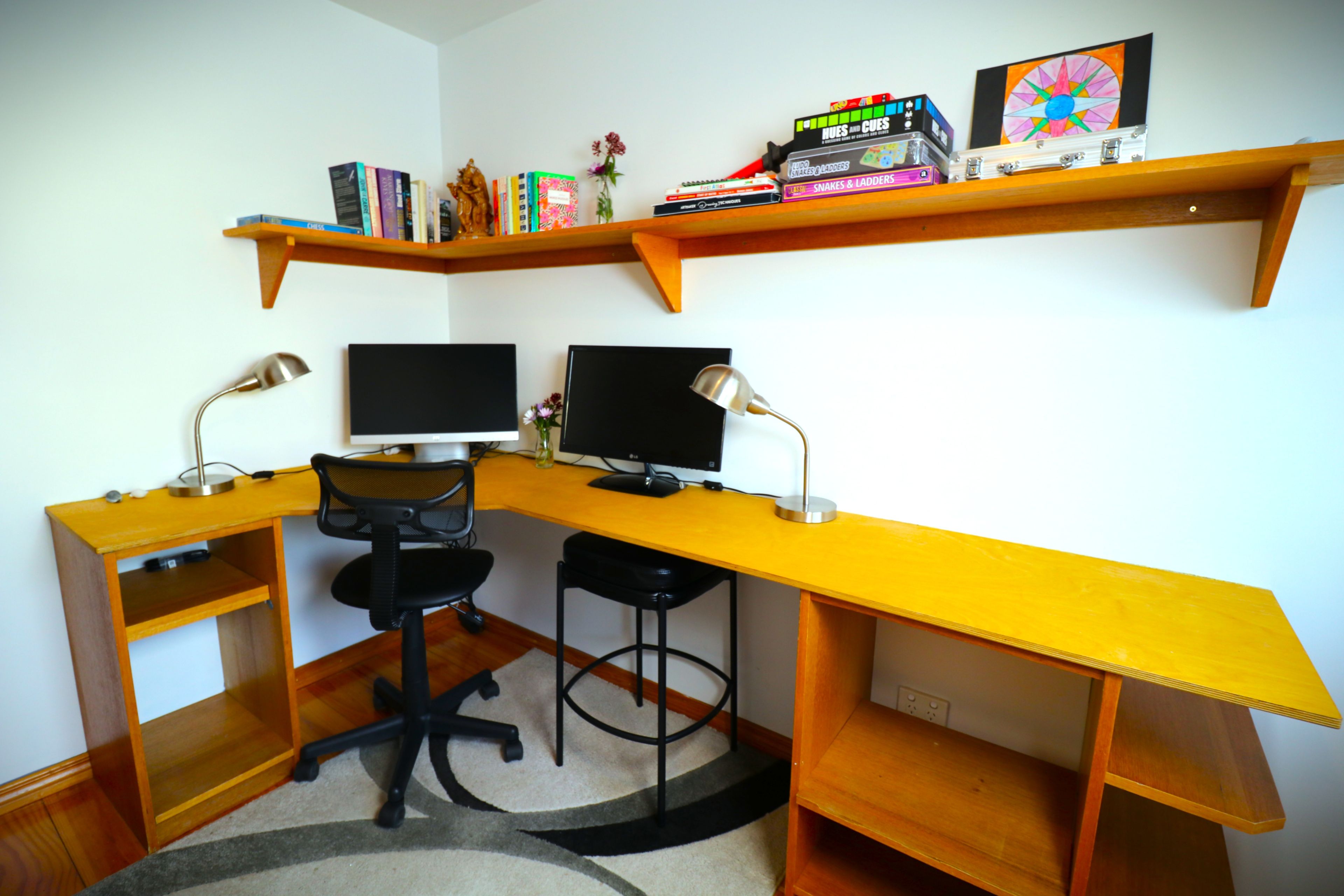 Un espace de travail d’angle équipé de deux écrans, d’une chaise et d’étagères contenant des livres et des objets décoratifs.