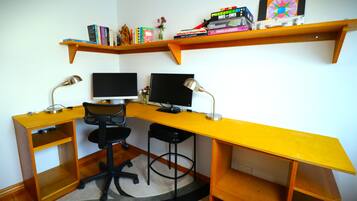 Un espace de travail d’angle équipé de deux écrans, d’une chaise et d’étagères contenant des livres et des objets décoratifs.