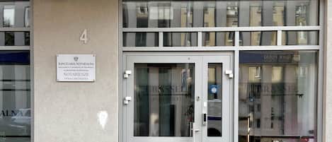 Entrada de un edificio con puerta de cristal, un letrero sobre la puerta y el reflejo de otro edificio en el cristal.