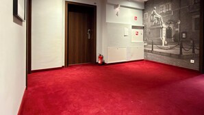 Un couloir avec un tapis rouge, une porte en bois et un mur orné d’une fresque en noir et blanc.