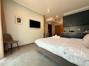A hotel room with a bed, a chair, a flat-screen TV, a kitchenette, and a door leading to another room. - Wrocław Główny Modern Studio (Wrocław)
