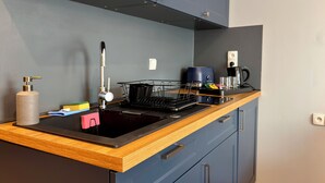 Une cuisine avec une plaque de cuisson noire, un plan de travail en bois, des placards bleus et une machine à café.