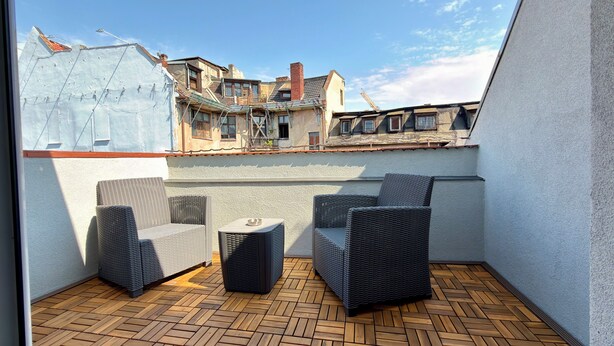 Une terrasse sur le toit, aménagée avec des meubles en osier et un plancher en bois disposé en motif chevrons.