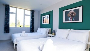 A hotel room with two beds, a small table, and a window with curtains. - #141 Coastal Apartment BournemouthBeach| Sleeps 10 (Bournemouth)