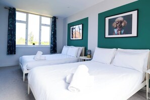 A hotel room with two beds, a small table, and a window with curtains. - #141 Coastal Apartment BournemouthBeach| Sleeps 10 (Bournemouth)