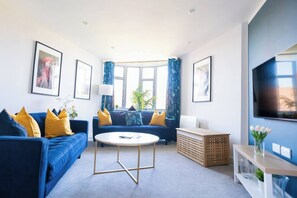 Un salon moderne avec un canapé bleu, une table basse ronde et un téléviseur fixé au mur.