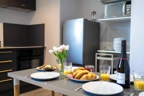 Une cuisine moderne avec une table à manger dressée pour le petit-déjeuner, comprenant des croissants, du jus d’orange et une bouteille de vin.