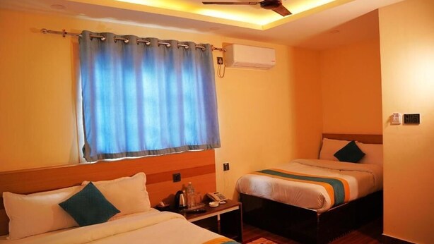 Quarto de hotel com duas camas, um ventilador de teto, um ar condicionado e uma janela com cortinas.