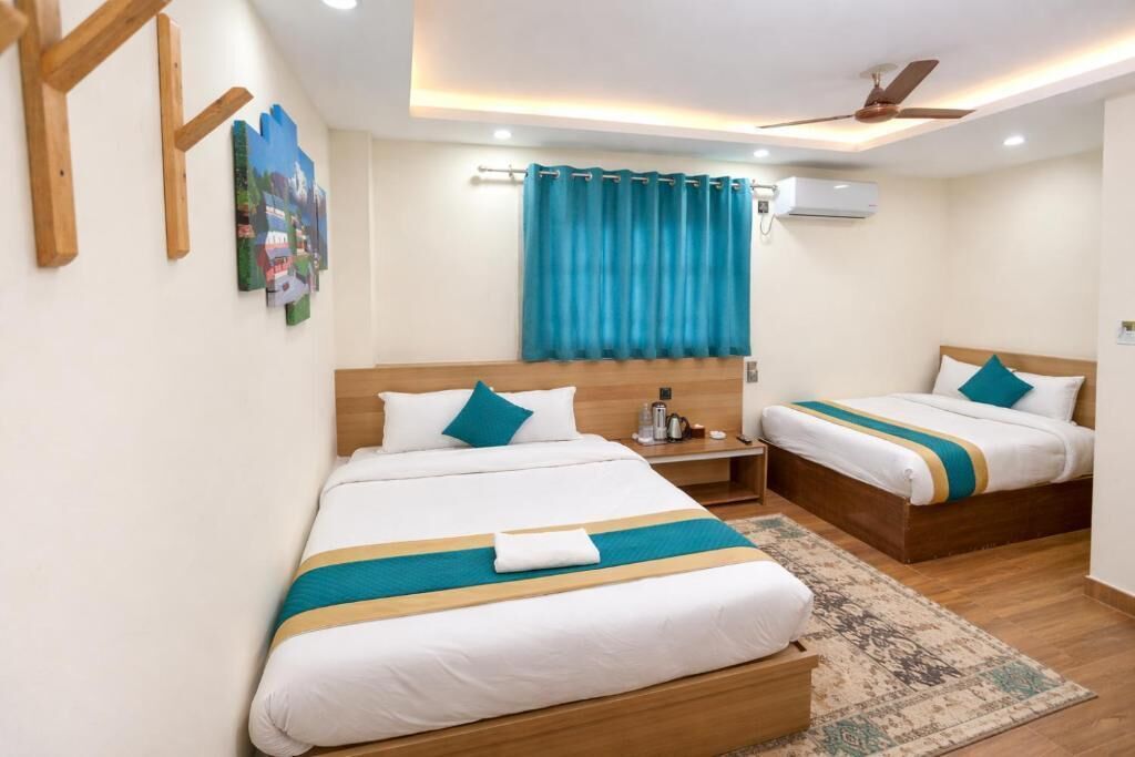 Habitación de hotel con dos camas, ventilador de techo, aire acondicionado y una alfombra estampada.